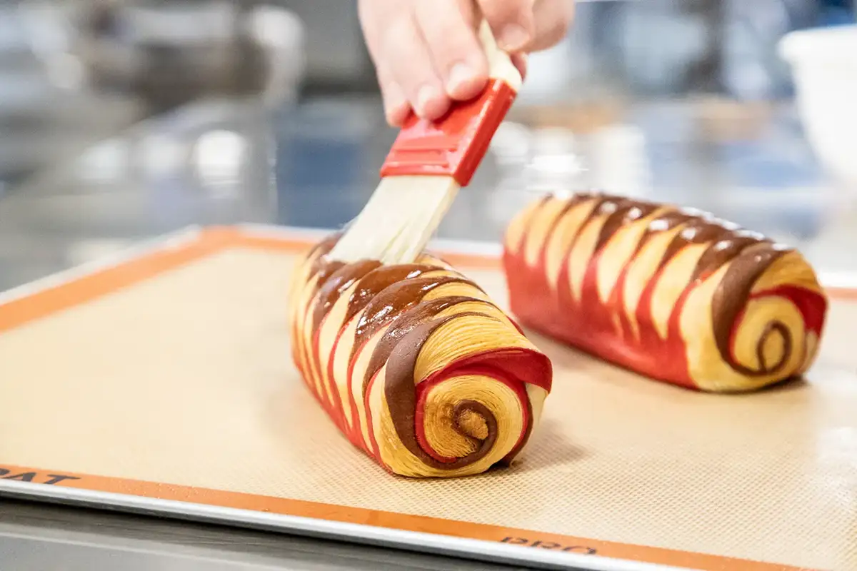 Brocha extendiendo crema de huevo pastelera sobre napolitanas