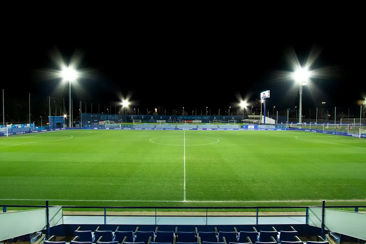 Fotografía de una vista frontal del campo de fútbol con las gradas vacías y focos simétricos