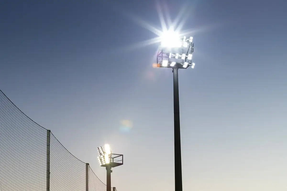 Fotografía de dos torres de focos recortadas sobre el cielo al atardecer en una ciudad deportiva