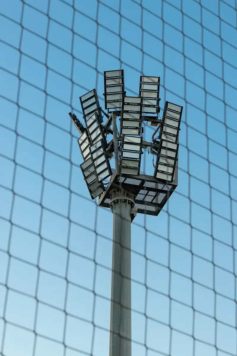 Fotografía de iluminación en crentro deportivo visto a través de la red perimetral del campo
