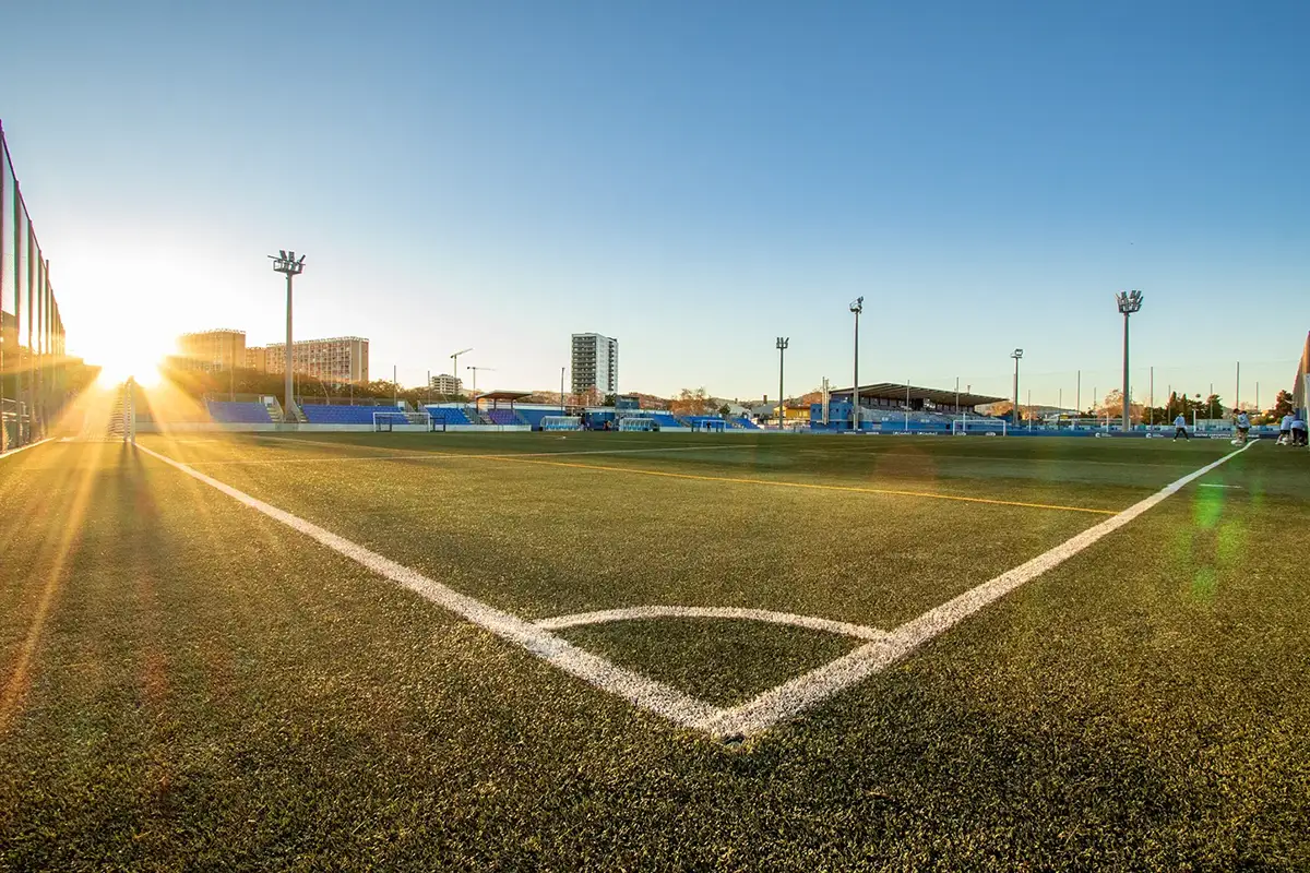 Fotografía desde la esquina del campo de fútbol al atardecer con el sol entrando en cuadro y largos dorados