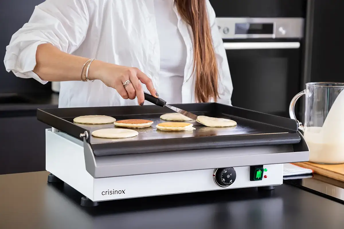 Mujer cocinando pancakes en una plancha eléctrica Crisinox en una cocina moderna