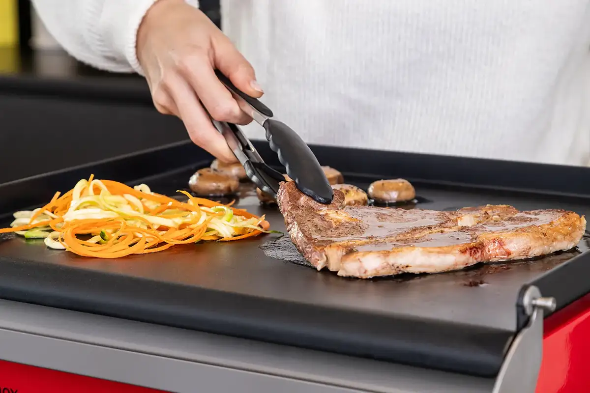 Detalle de verduras y carne cocinándose en una plancha Crisinox vista en primer plano