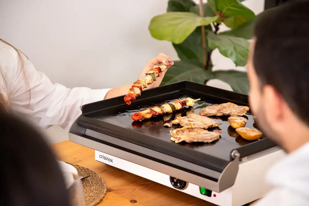 Mujer mostrando una brocheta recién hecha sobre una plancha Crisinox para el hogar