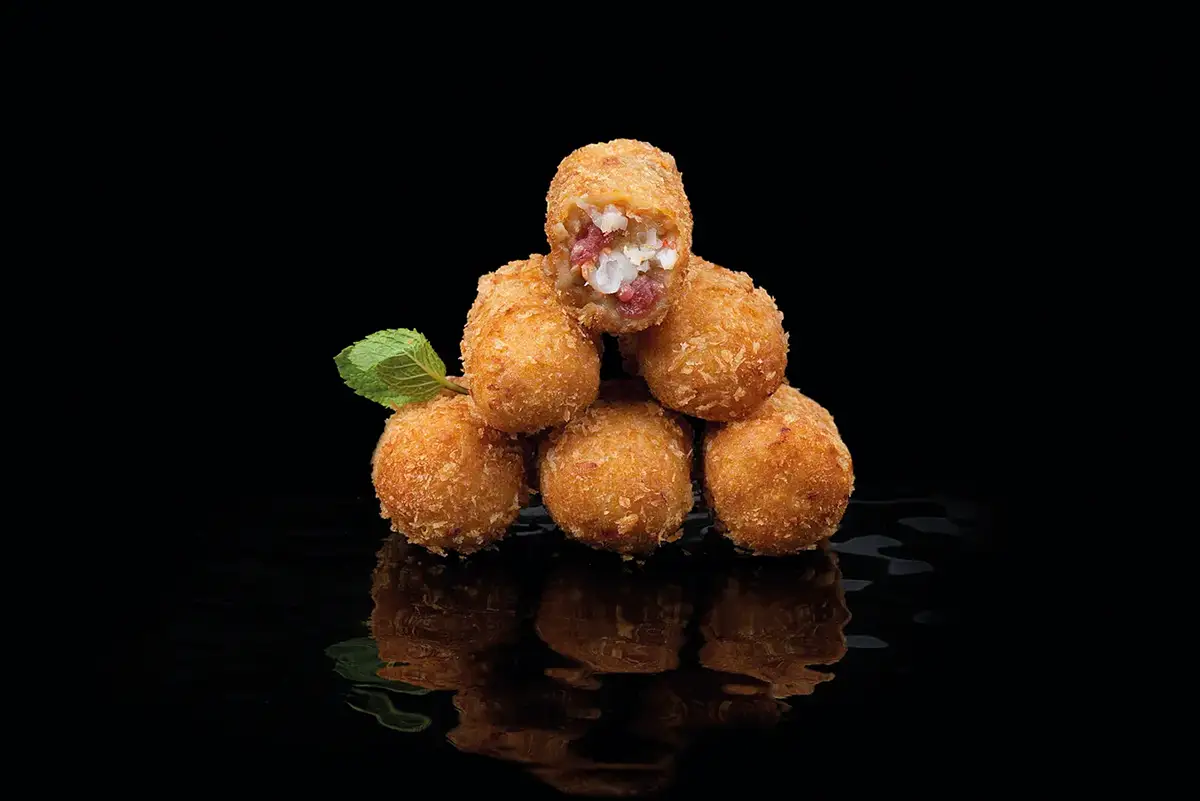 Fotografía gastronómica de torre de croquetas doradas con relleno visto sobre fondo negro