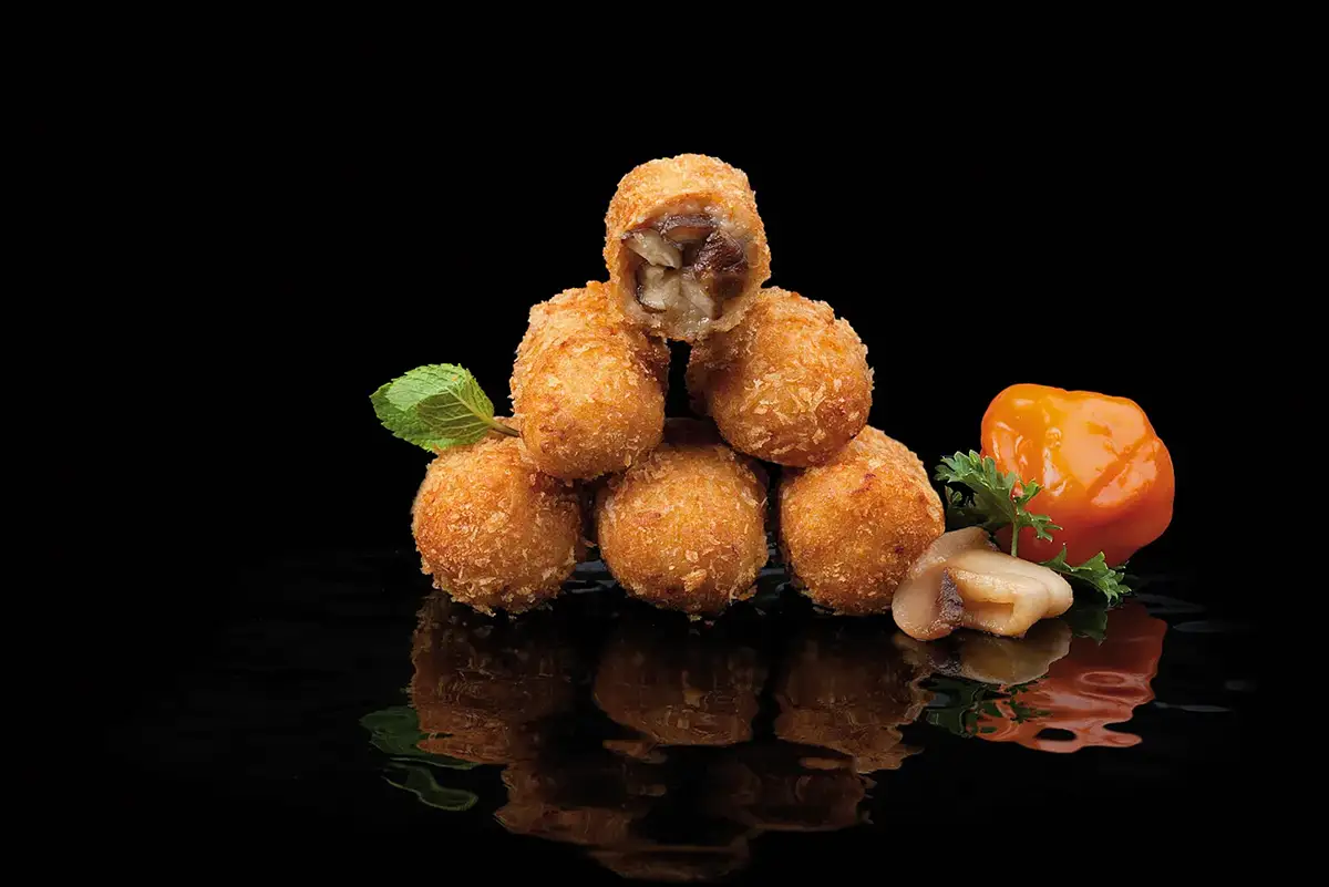 Fotografía gastronómica de croquetas acompañadas de setas y pimiento sobre fondo negro