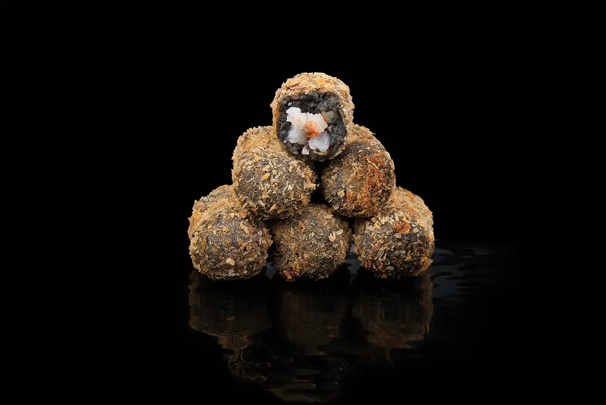 Fotografía gastronómica de croquetas negras rellenas de marisco con reflejo en fondo negro