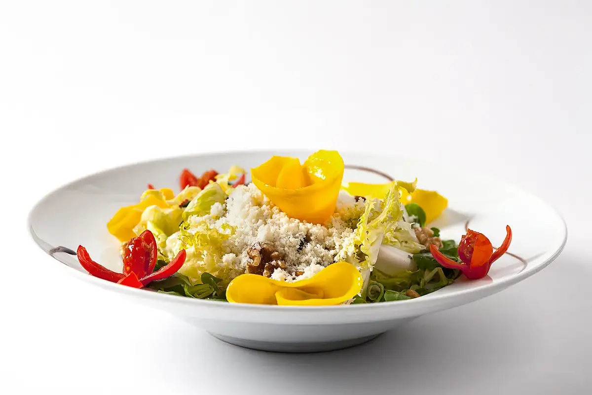 Fotografía para carta de resturante de una ensalada colorida con flores de mango y frutos secos sobre fondo blanco
