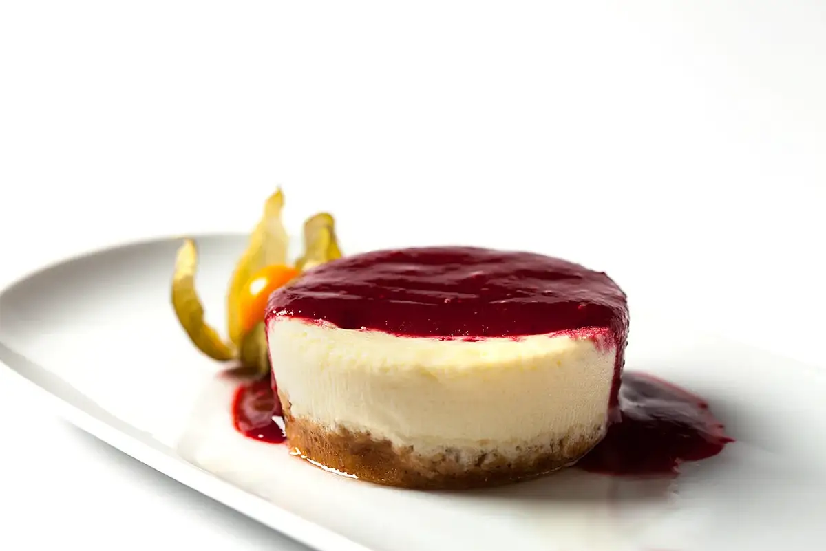 Fotografía de tarta de queso individual con coulis de frutos rojos