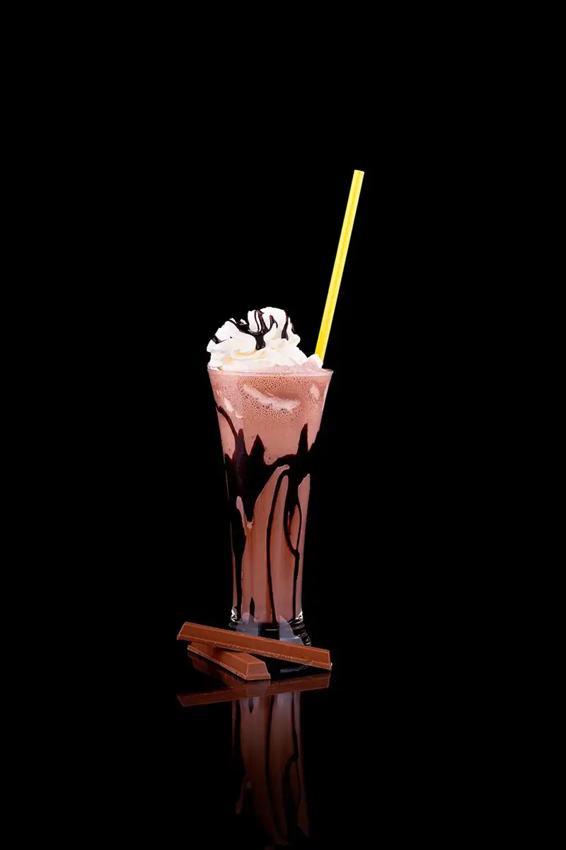 Batido de chocolate con nata y sirope en vaso alto sobre fondo negro