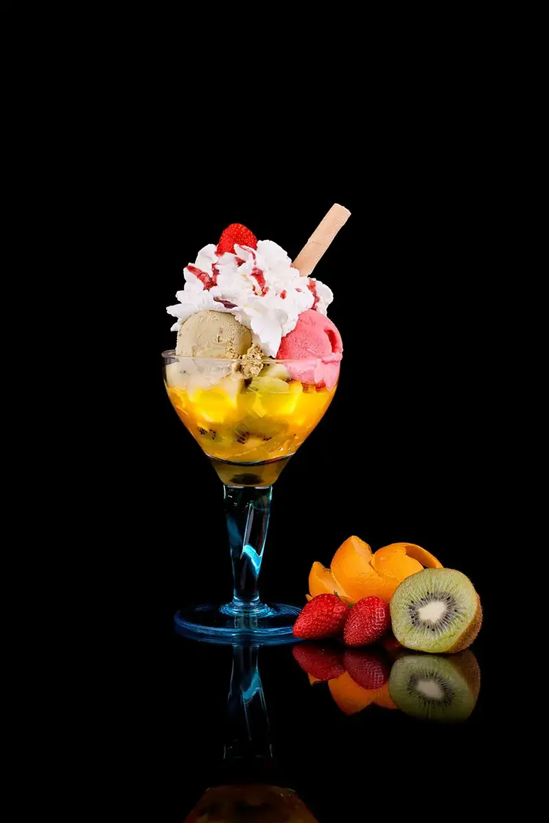 Copa helada con bolas de helado, frutas frescas y nata sobre fondo negro