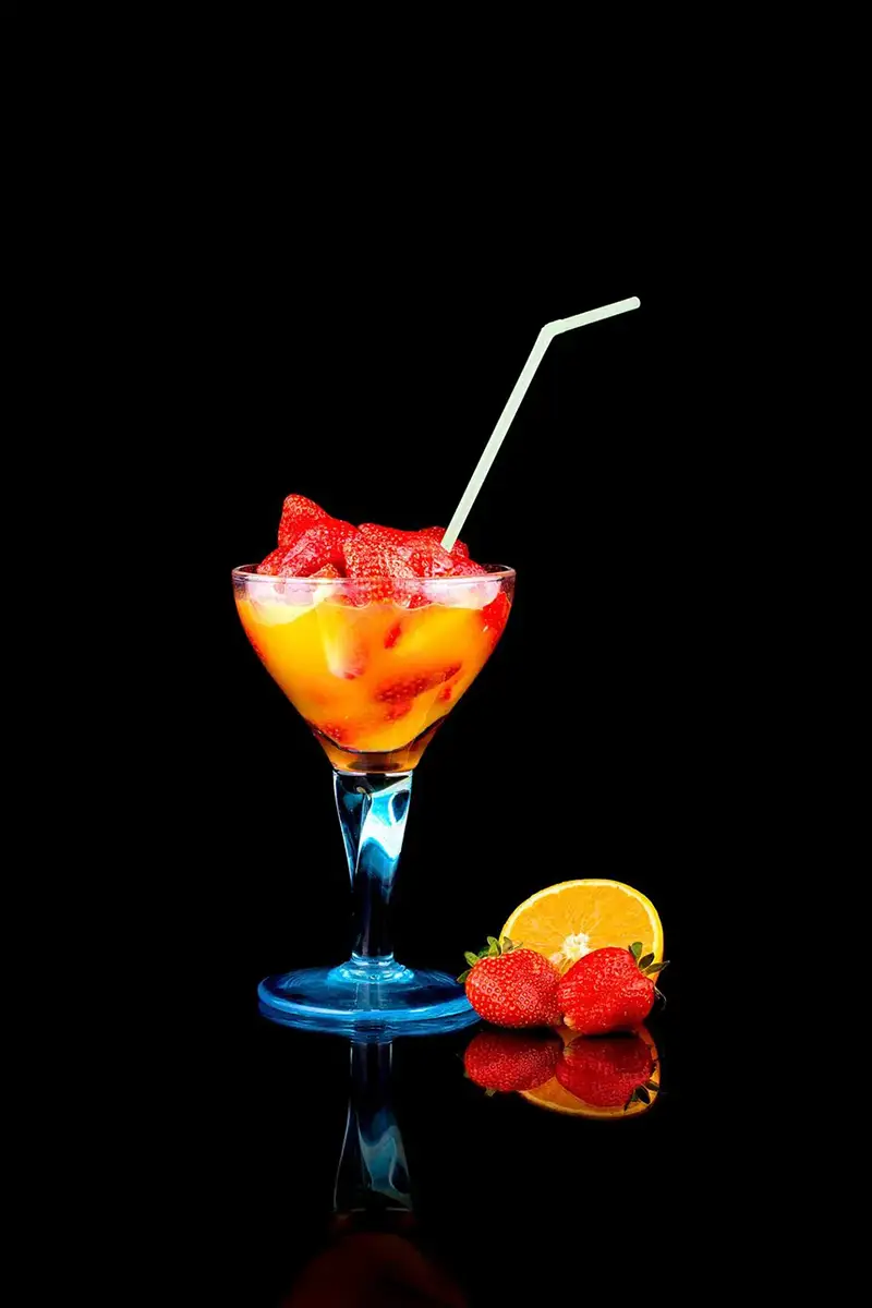 Cóctel de frutas con fresas y naranja en copa alta sobre fondo negro